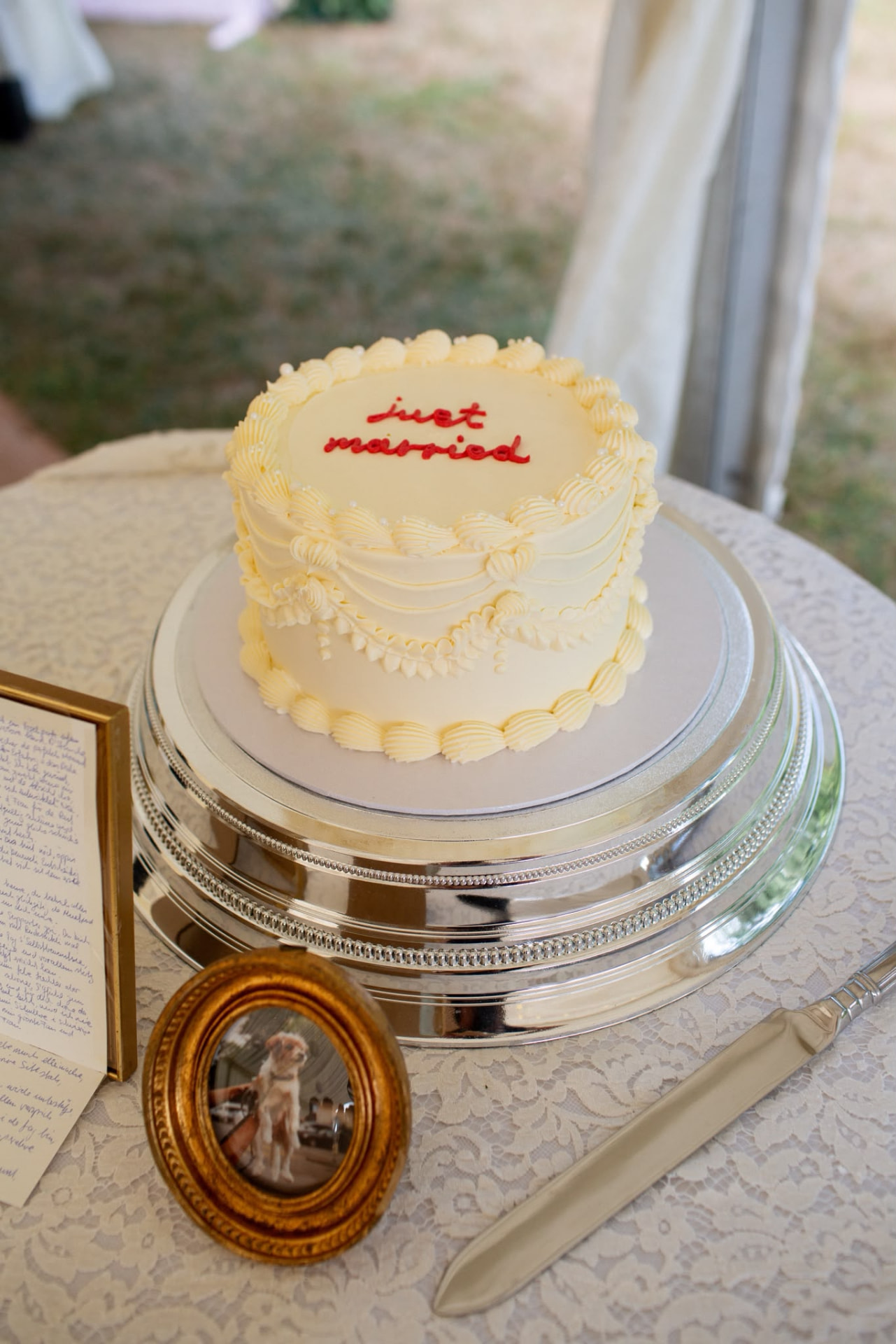 Just married wedding cake on a silver stand beside handwritten notes and a framed photo of the couple's dog