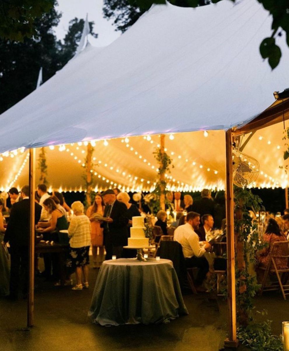 An evening marquee wedding reception glowing with warm string lights and candlelit tables